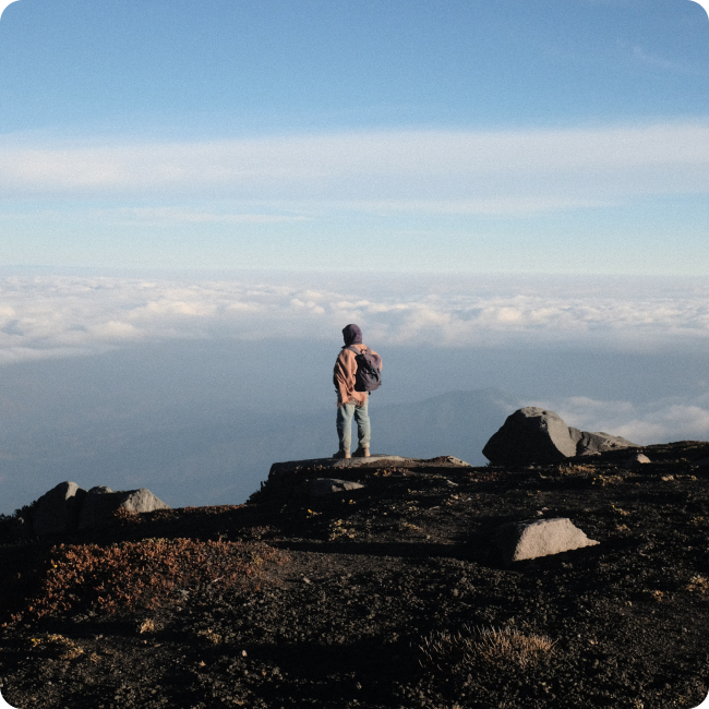 Person standing at the top of a mountain overlooking the clouds